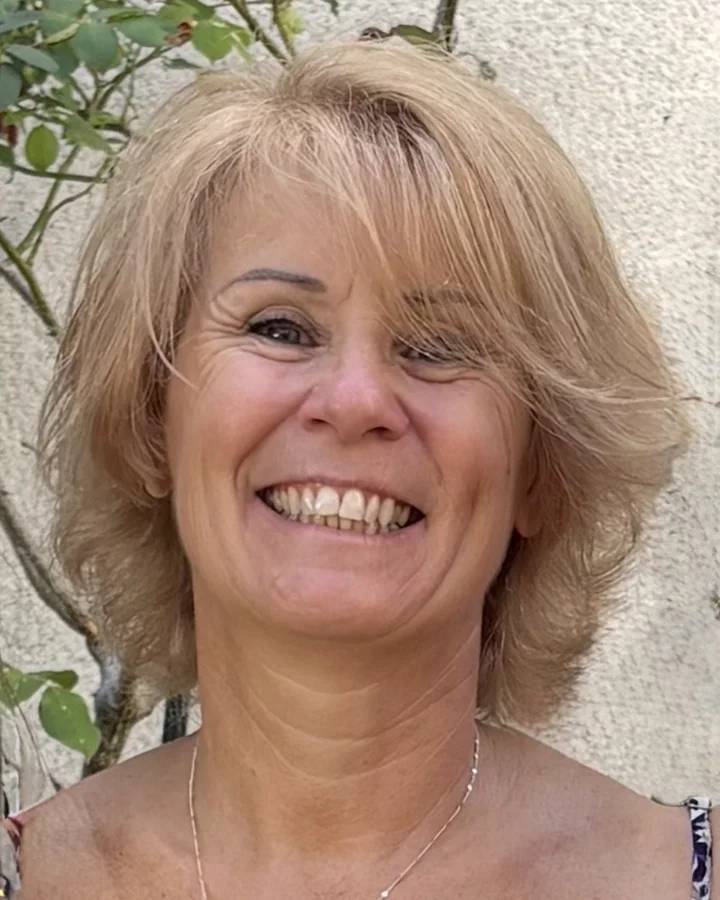Valérie Parisset, souriante, devant un mur clair où grimpe un rosier